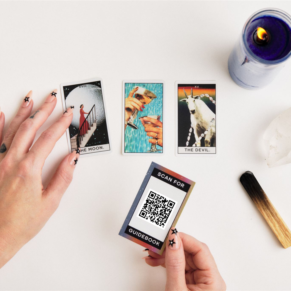Hand holding a card to scan for guidebook and 3 mini tarot stickers in a tarot reading scene with candle and palo santo