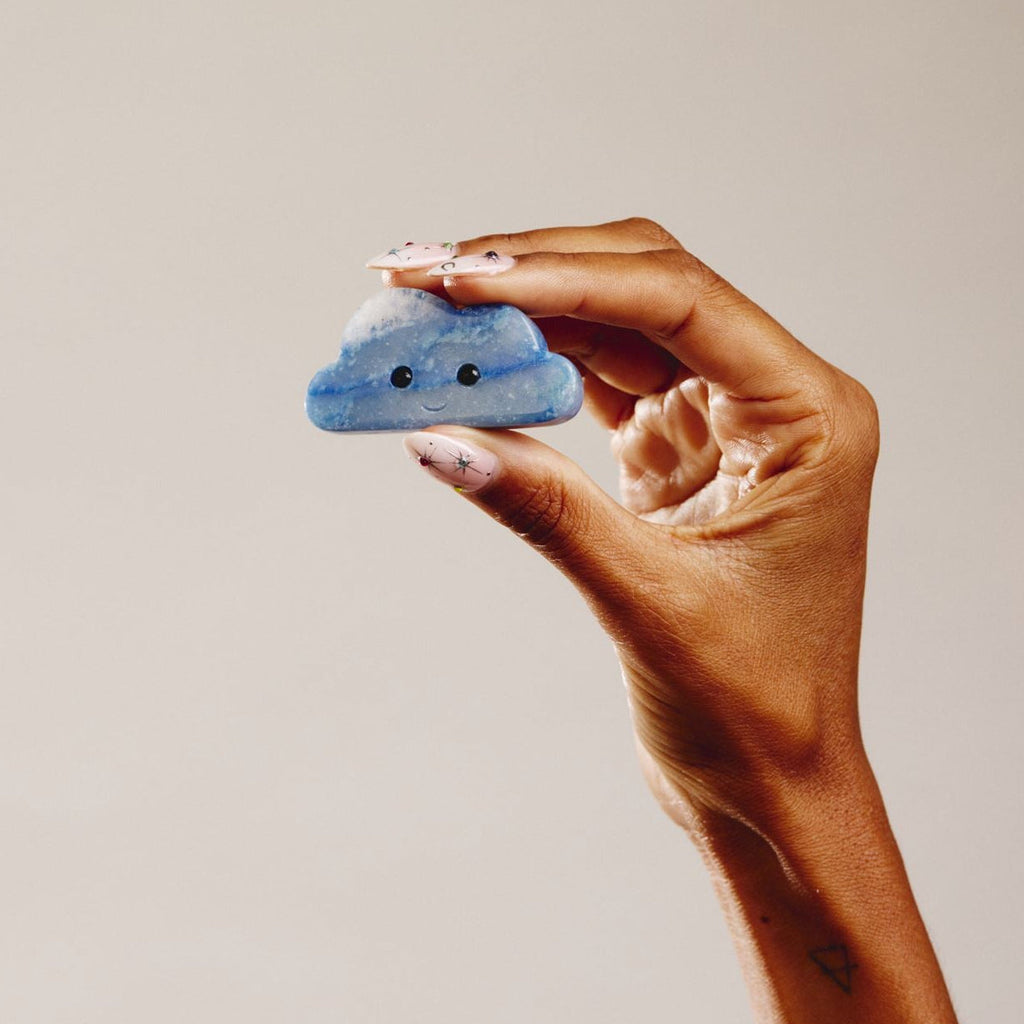 Hand holding a blue aventurine crystal in the shape of a cloud with a smiley face 