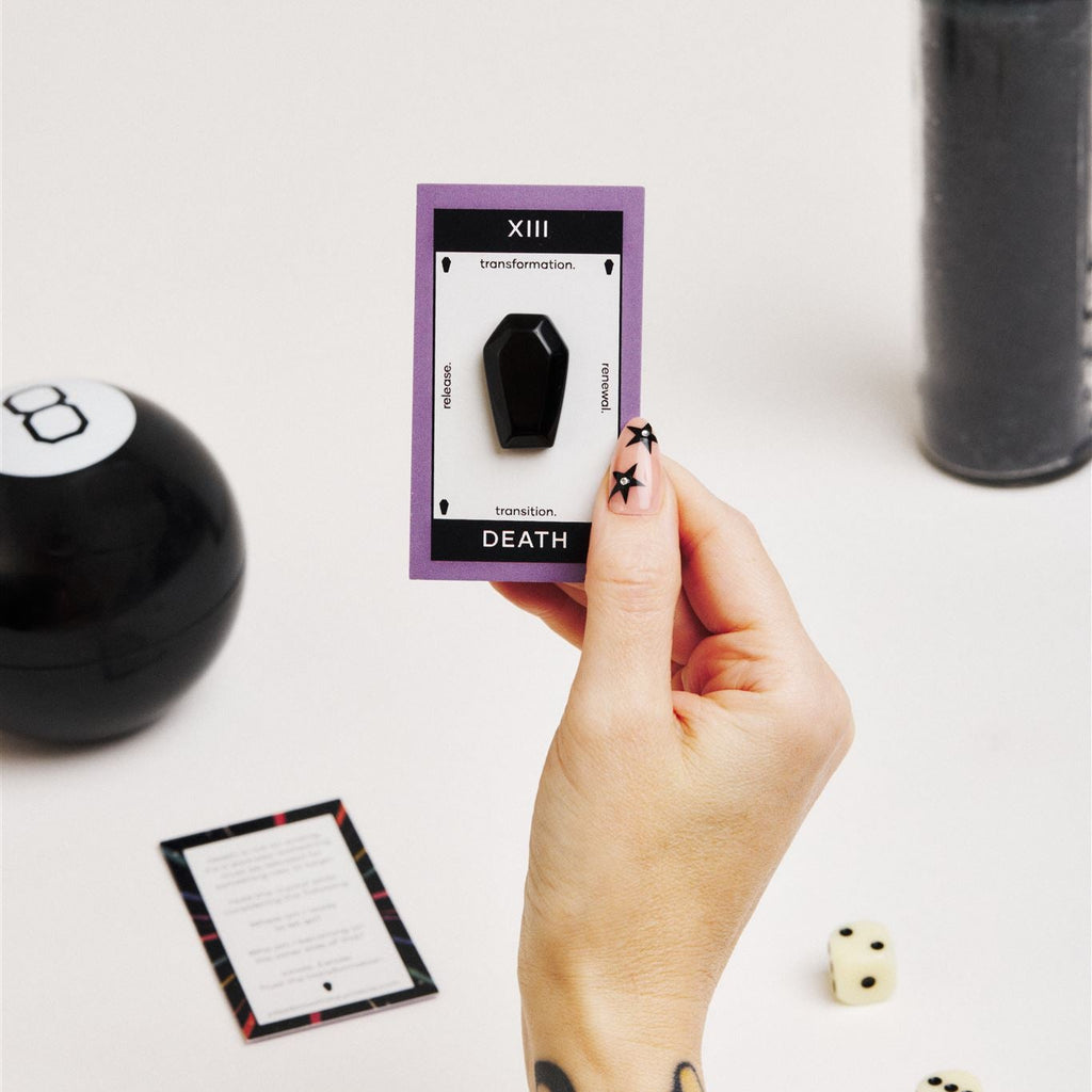 hand holding card with black coffin crystal surrounded by tarot reading supplies