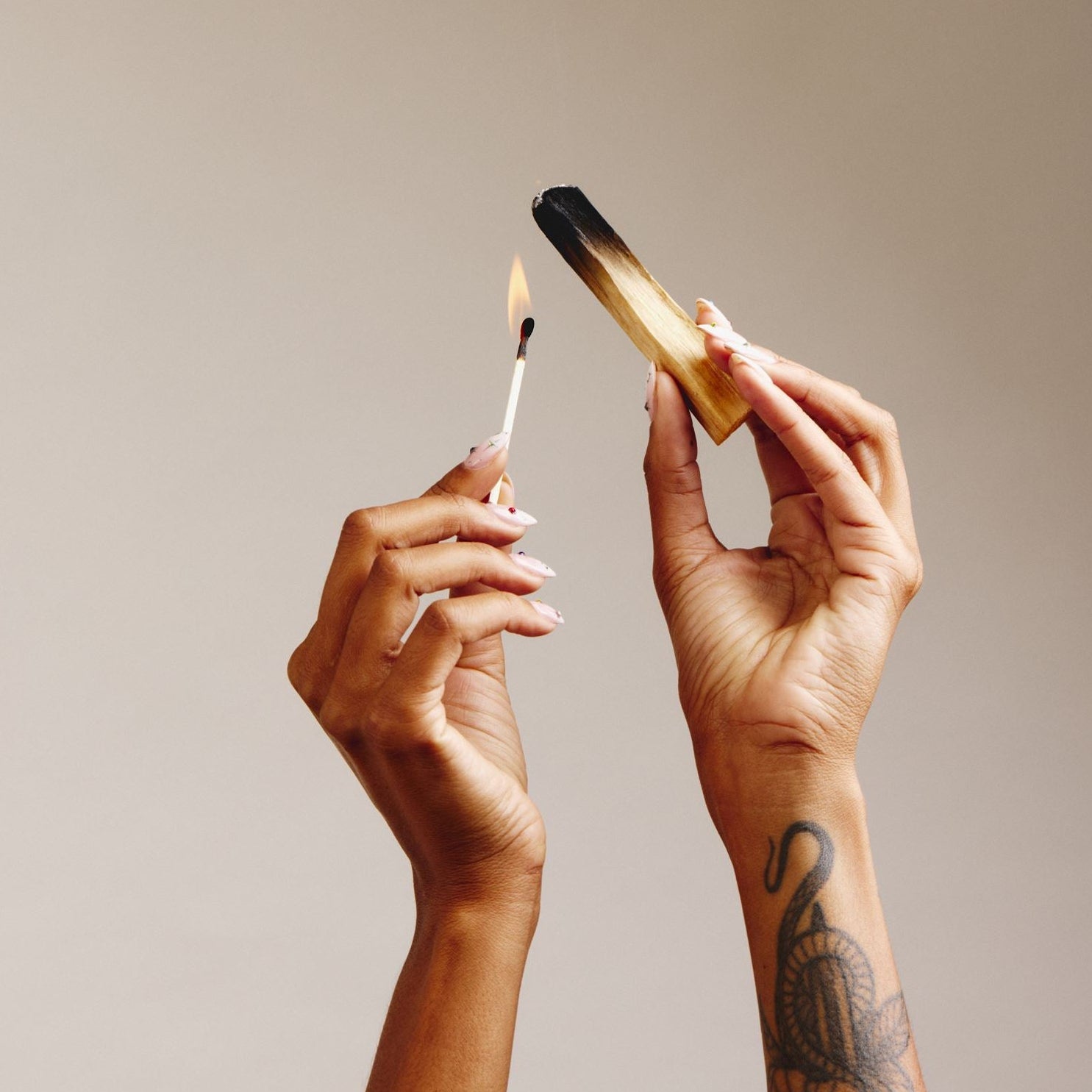two hands, one hand holding a lit match and one hand holding a stick of palo santo to be lit