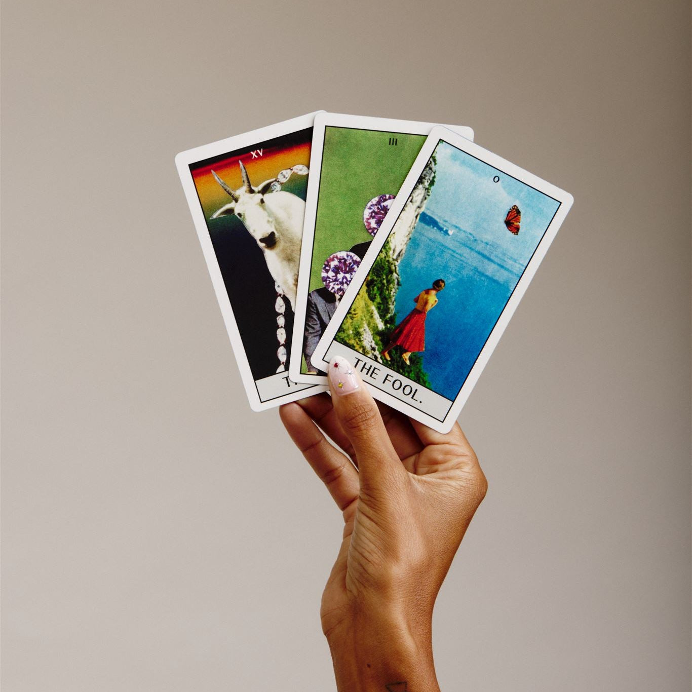 Hand holding 3 tarot cards, the fool, the devil and the  of pentacles or diamonds