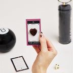hand holding a card with a heart shaped crystal surrounded by tarot reading supplies