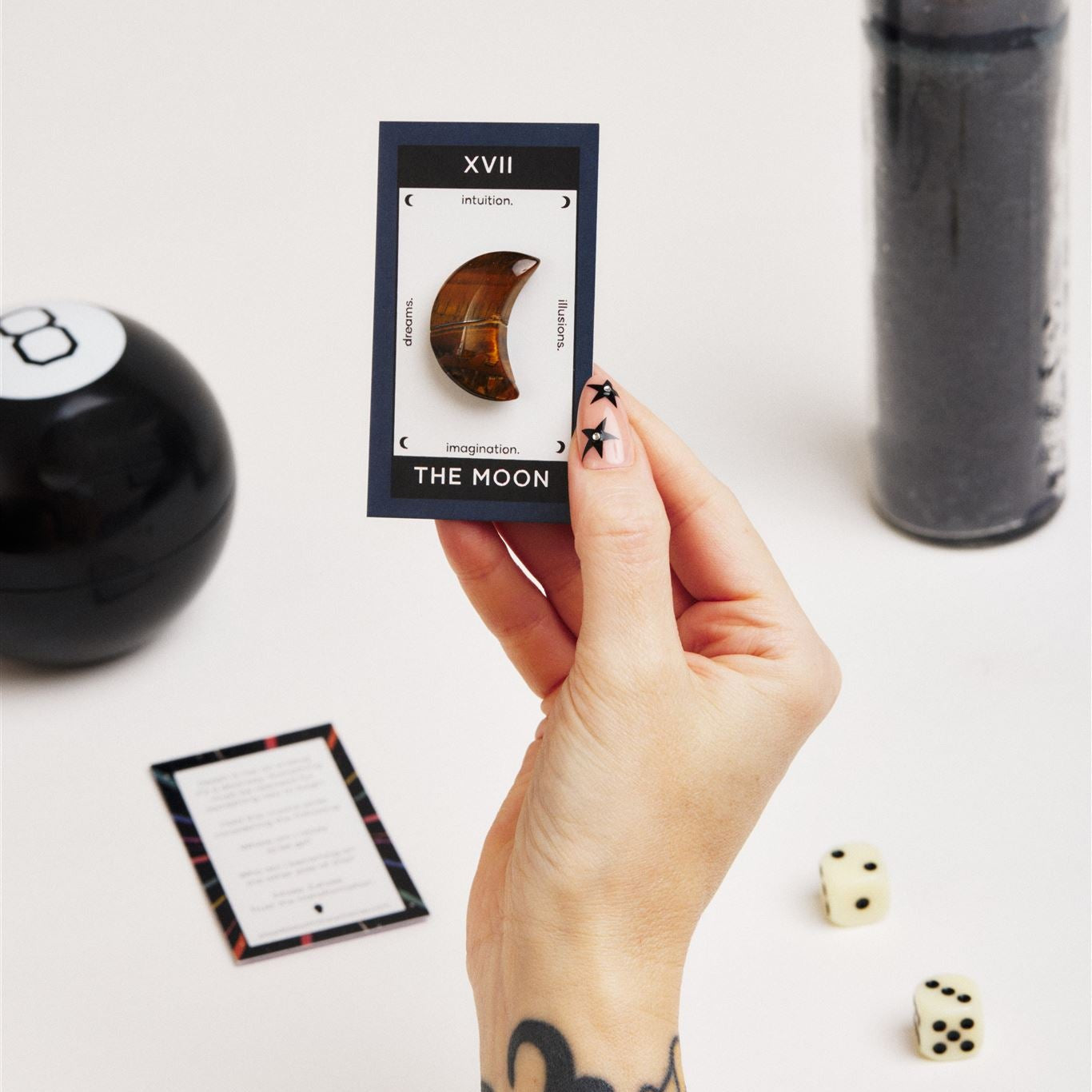 hand holding a card with a tiger eye moon surrounded by tarot reading supplies